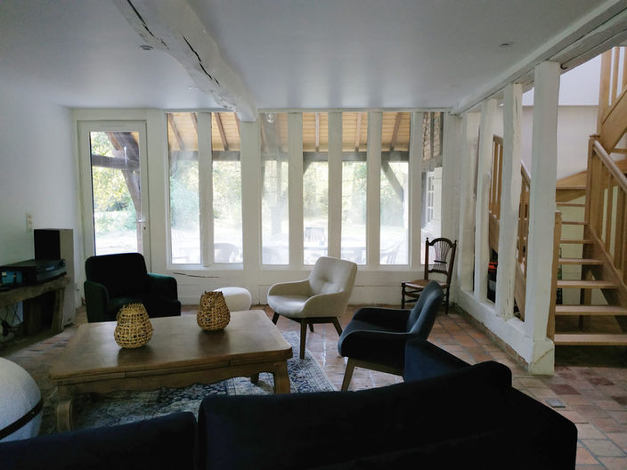 Salon avec canapés et fauteuils avec la verrière en arrière plan qui donne sur la forêt