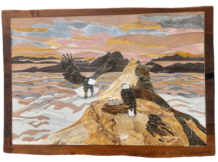 Cut stone artwork of two bald eagles on rocky mountaintop above clouds, one in flight and one standing near a nest with eaglets under a colorful sky.