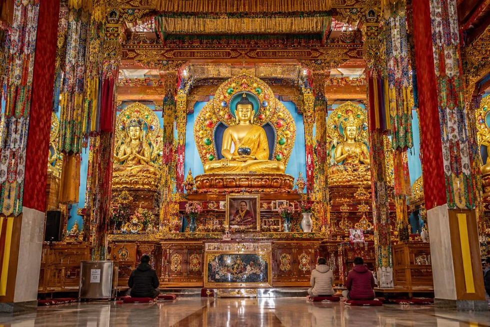  Tsuglagkhang Complex (Dalai Lama Temple) Three worshippers sit before golden Buddha statues in a richly decorated temple with colorful pillars and altar.