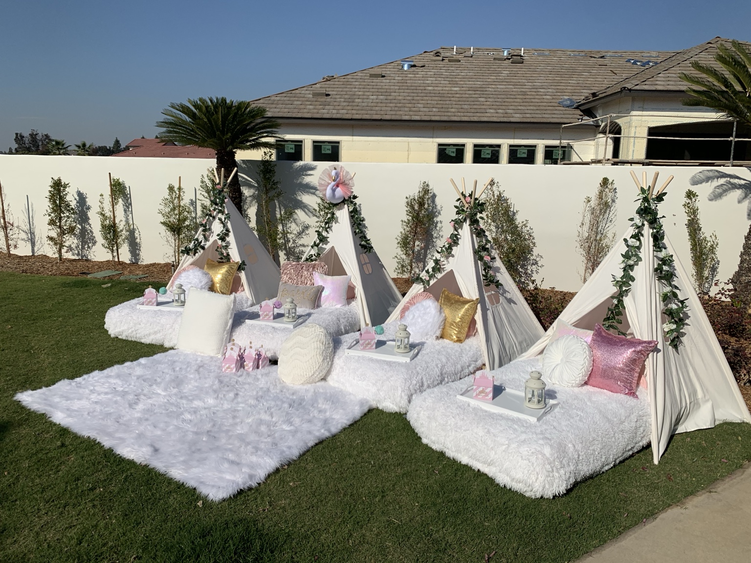 White teepee sleepover setup on a backyard lawn