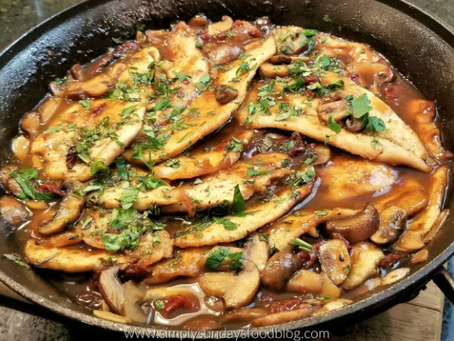 Chicken Marsala in a skillet with mushrooms and fresh herbs, glistening in a savory brown sauce. Warm kitchen setting evokes a hearty meal.