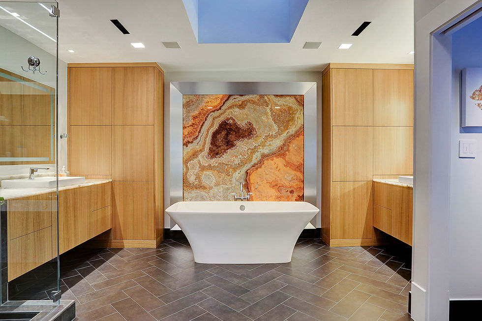 Light wooden bathroom with black floors with a white tub centered under a large orange onyx marble art piece