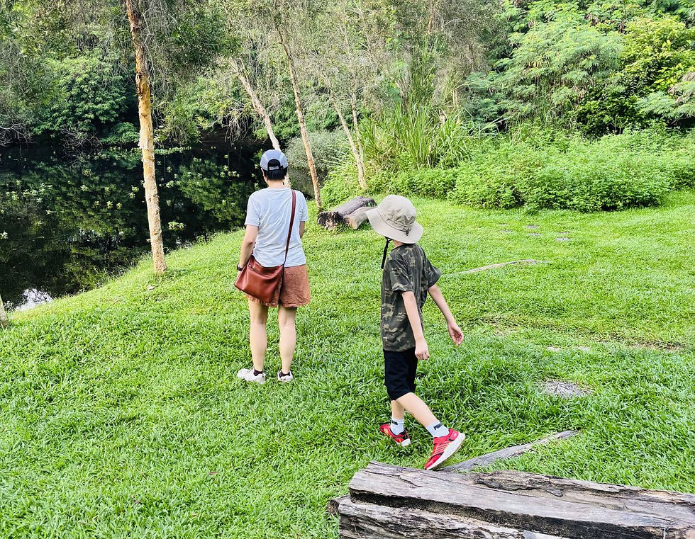 A woman and a child standing with their backs to the camera in a grassy area surrounded by trees.