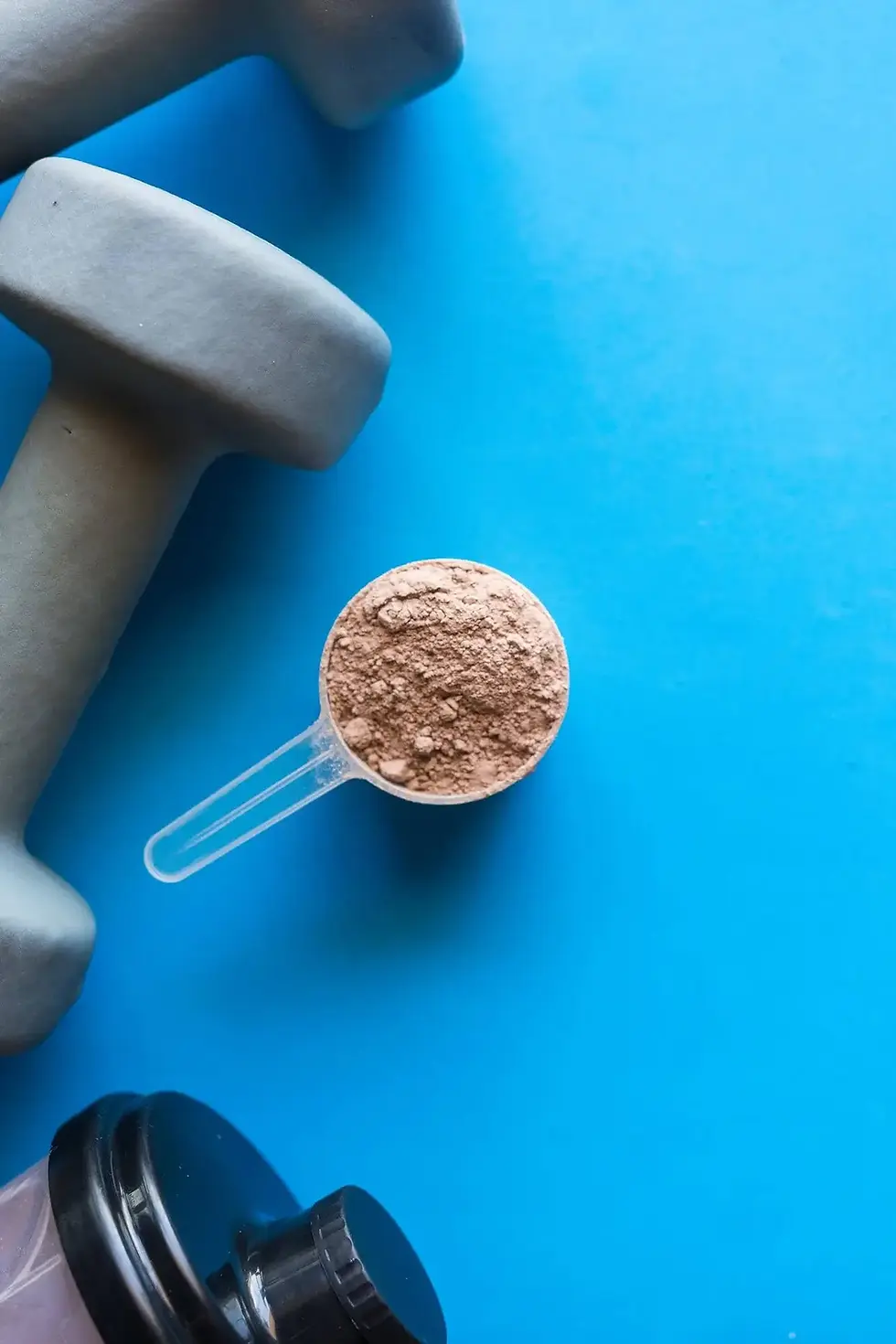 Scoop of powder beside dumbbells on a blue background