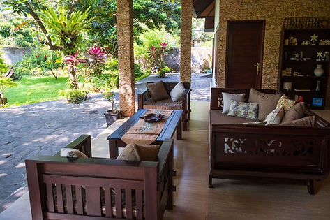 Ruang keluarga terbuka beratap di Vila Dua Kamar Tidur dengan Taman, dengan sofa kayu, meja kopi, dan pemandangan taman tropis.