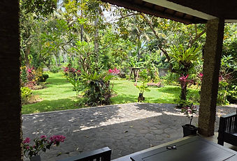 Pemandangan taman tropis yang tenang dari teras pribadi vila, dengan halaman hijau, tanaman berbunga, dan pepohonan rindang di Bondalem Beach Club.