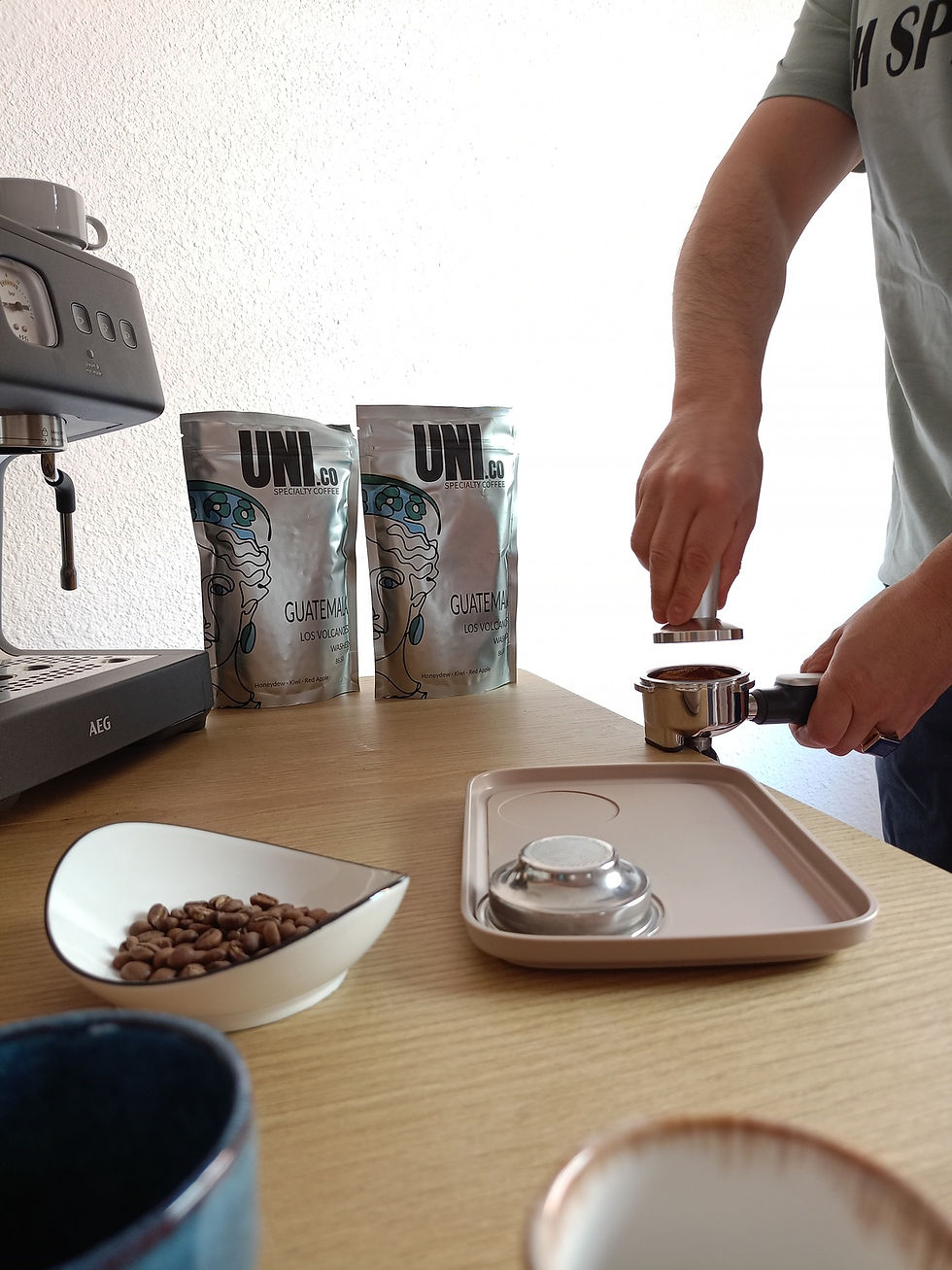 Hand-tamping the ground coffee with a professional tamper on a light wooden table.