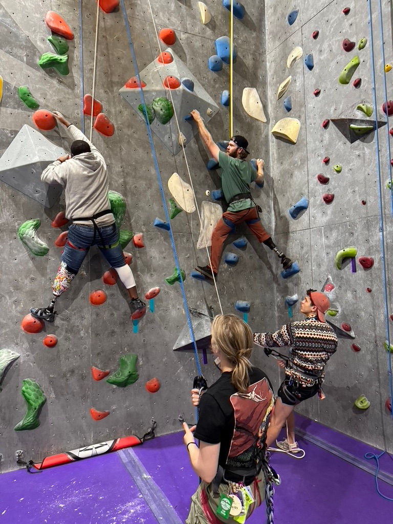 volunteers at Aiguille Climbing belaying for an adaptive climbing event