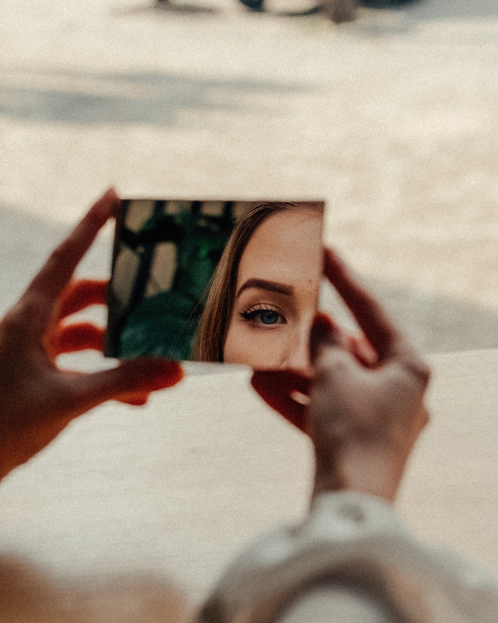 Woman holding a small mirror, revealing part of her face in a moment of self-reflection.