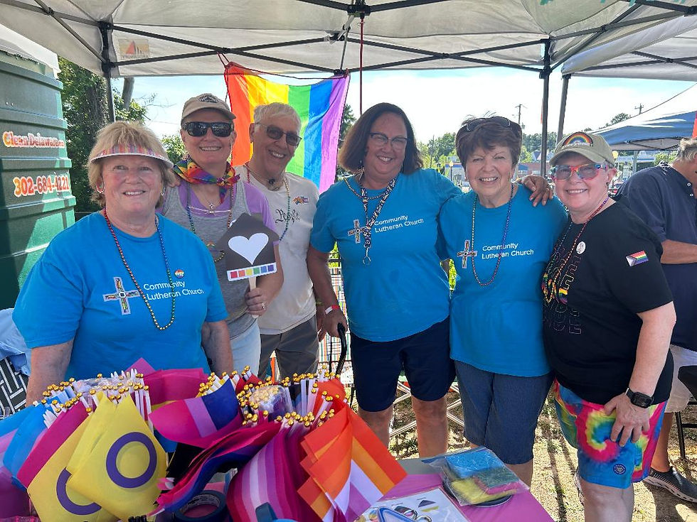 a group of people in t-shirts that say Community Lutheran Church at a Pride festival vending table covered in rainbow decorations