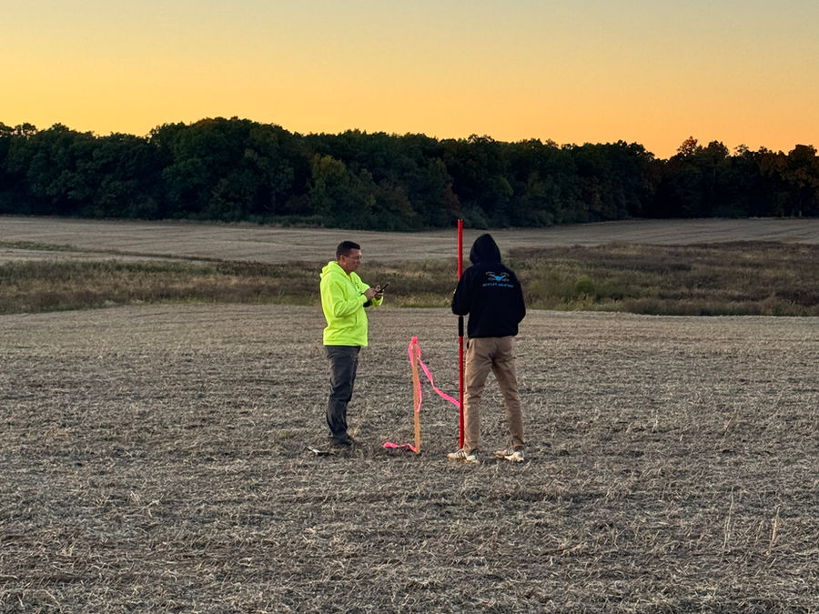 Two survey crew members setting control with a survey pole in a field at dusk