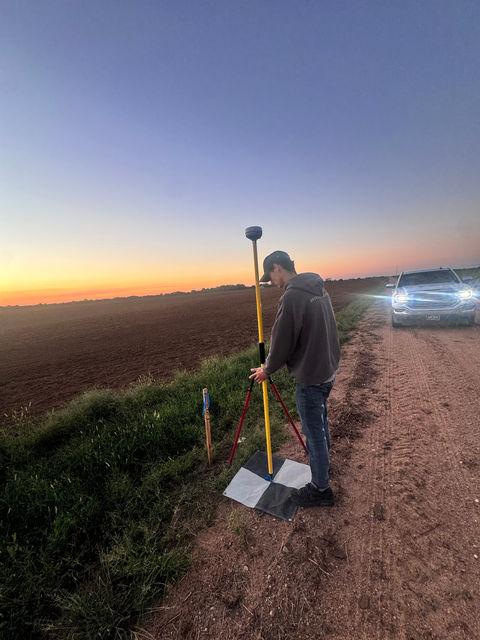 A surveyor standing with a GNSS rover pole at dusk