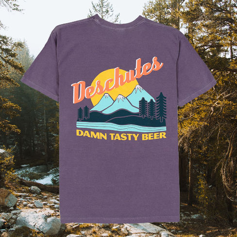 Purple tee with blue mountains, green tees, and a yellow sun. "Deschutes" and "Damn tasty beer" are printed.