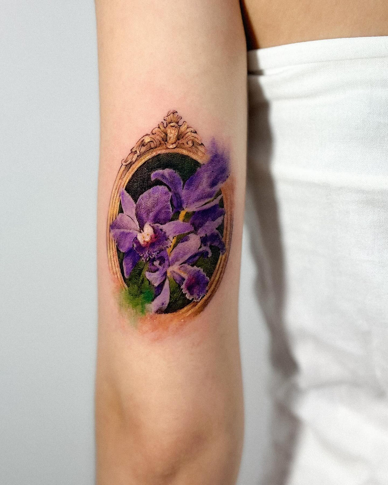 Tatuagem botânica com composição de flores roxas envoltas por uma moldura, feita pela artista Fernanda Calegari no Studio Atmos em Moema - SP