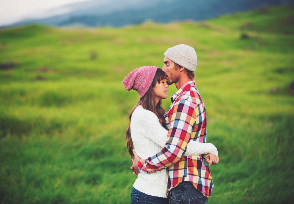 a man and woman hugging in a field with mountains in the background