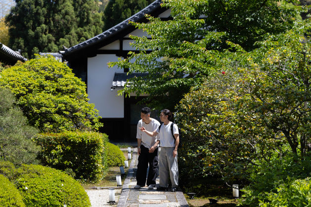 2 friends walking around the green gardens of a shrine in Kyoto, Japan