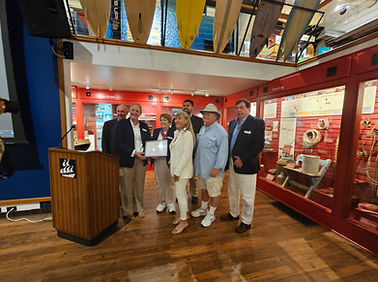 Captain Christine Healy surrounded by a group of adults holding a wooden plaque at the commissioning of Mystic Whaler