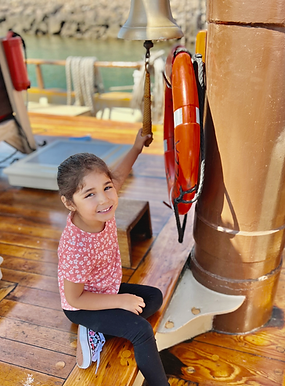 A smiling small child holding the bell pull on Mystic Whaler's deck bell.