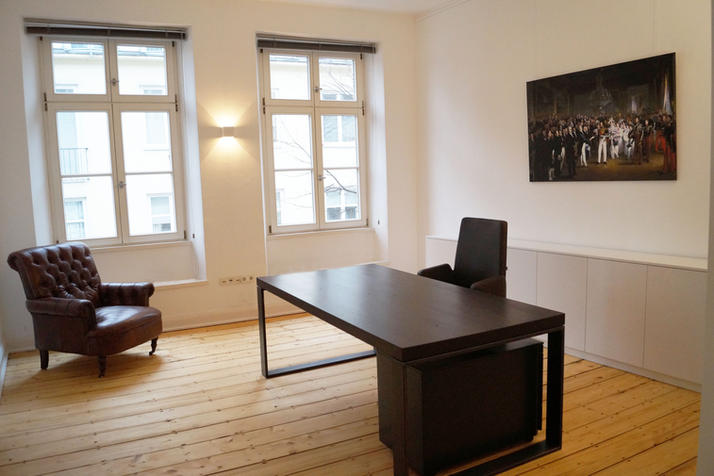 schwarzer Schreibtisch mit Bürostuhl. Gemütlicher Sessel vor Fenster.
