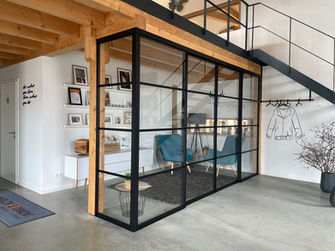 Bild von einem Raum mit  Loftschiebetürensystem. Glaswand mit schwarzen Rahmen, Holzkonstruktion