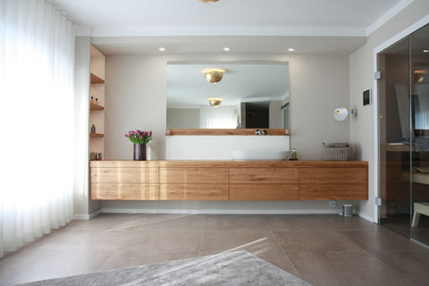 Modernes Badezimmer mit Holz-Waschbeckenunterschrank von einer Raumecke zu anderen, großer Spiegel und Blumen vor einem Einbauregal; Hergestellt von Holzvisionen