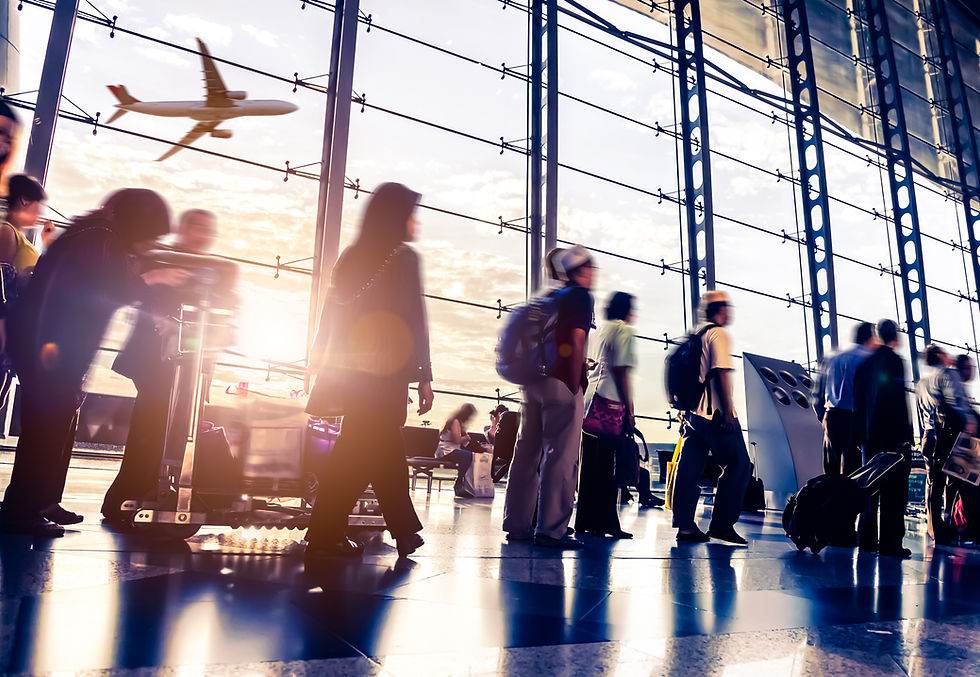 People walk in an airport terminal with luggage carts. A plane flies outside large windows. Sunlight creates a warm, busy atmosphere.