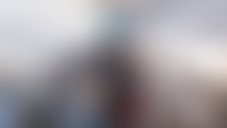 A view of the aisle of a passenger aircraft. A flight attendant moves down the corridor, facing away from the camera; passengers also face forwards.