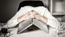 A man hiding his head under his laptop