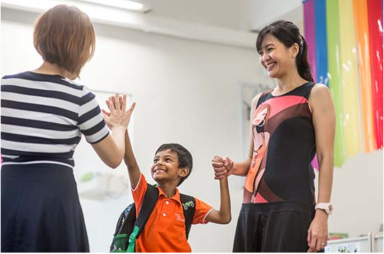A happy boy high-fives his teacher while holding his mother’s hand on a cheerful school day.