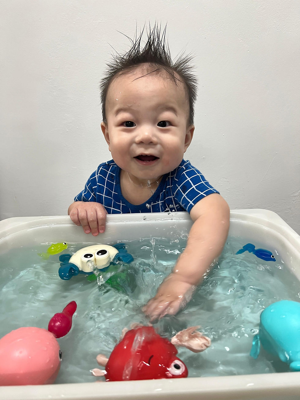 A happy baby splashes water with colorful bath toys.