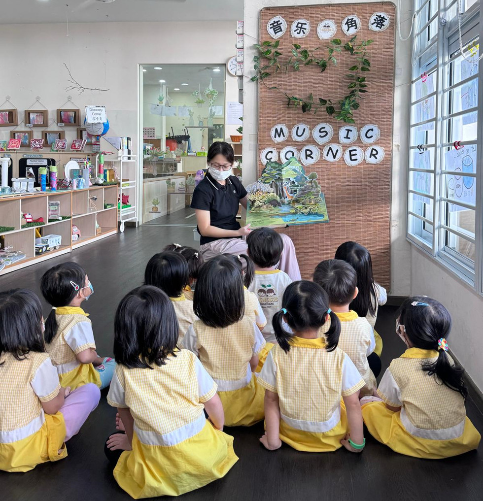 A teacher reading a story to children gathered at the classroom’s music corner.