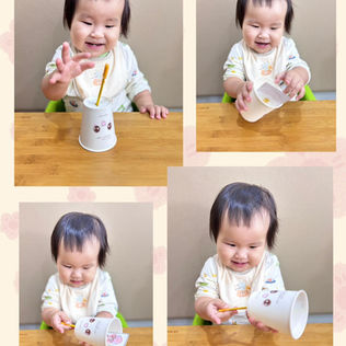 A happy baby exploring a cup and pencil.