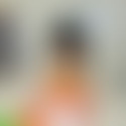 A child carefully decorates a paper face craft on an orange background.