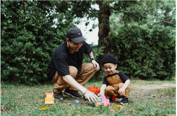 A man and child play with toy vehicles on the grass.
