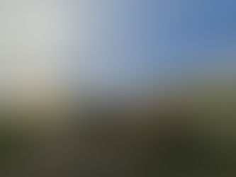 Tractor with red equipment on grassy field during sunset; hills and trees in background under a cloudy sky, creating a serene rural scene.