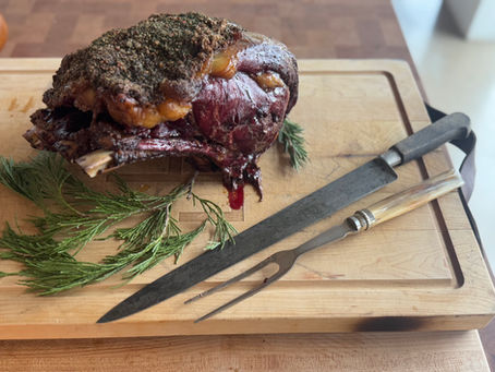 Roast beef with herb crust on a cutting board, garnished with rosemary. Knife and fork beside it. Warm lighting creates a cozy mood.