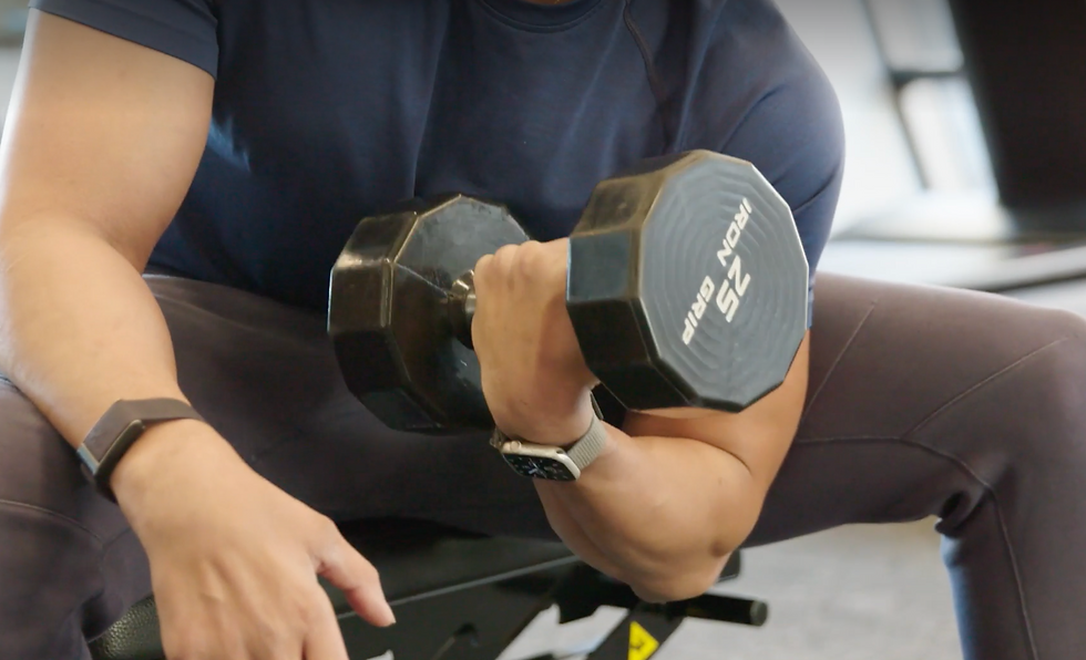Man doing concentration wrist curls with dumbbell on bench in gym