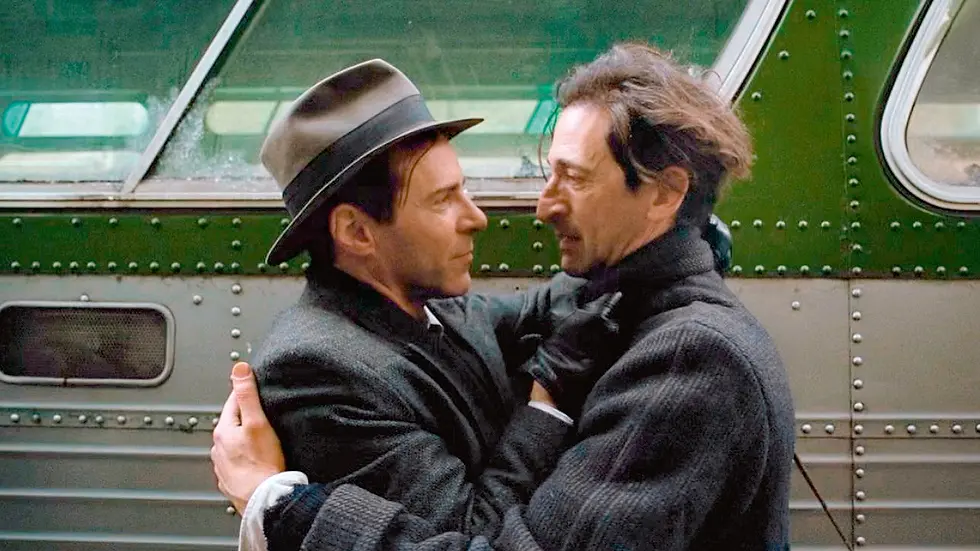 two mens hugging, brown hair, grey coat, white shirt, black sweater, beige hat, old van, green and grey van, black gloves