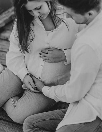 Eine Schwangere sitzt auf dem Boden eines Fotostudio und wird von Ihrem Mann umarmt. Sie schauen gemeinsam auf den Bauch der Schwangeren und Alexandra Specker hat diese Emotion eizigartig fotografiert