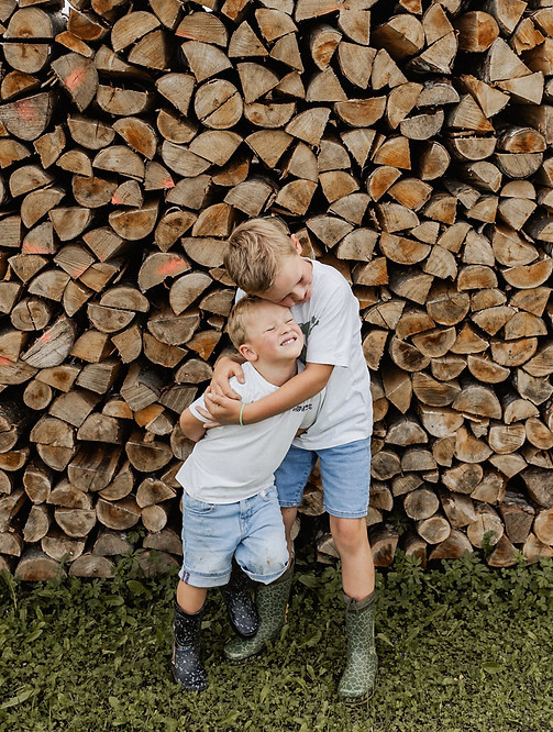 Das Bild ist in Spaichingen fotografiert und zeigt zwei Kinder, die vor einer Holzwand stehen und sich umarmen, Die Kinder lachen und haben Vertrauen zur Fotografin