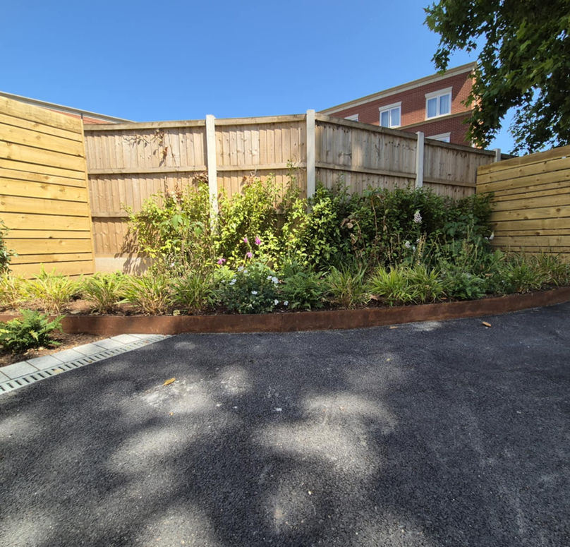 Curved weathering steel flower bed border with planting, tarmac, and wooden slatted screening