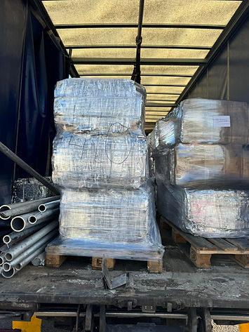 Stacks of plastic-wrapped pallets on a truck bed, surrounded by metal pipes