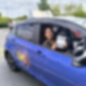 A smiling female learner driver sits in a blue Universal Motoring School car holding her test pass certificate