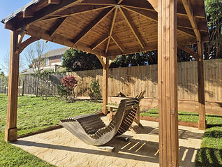 Octagonal wooden gazebo over a paved area featuring a unique wooden rocking lounger chair