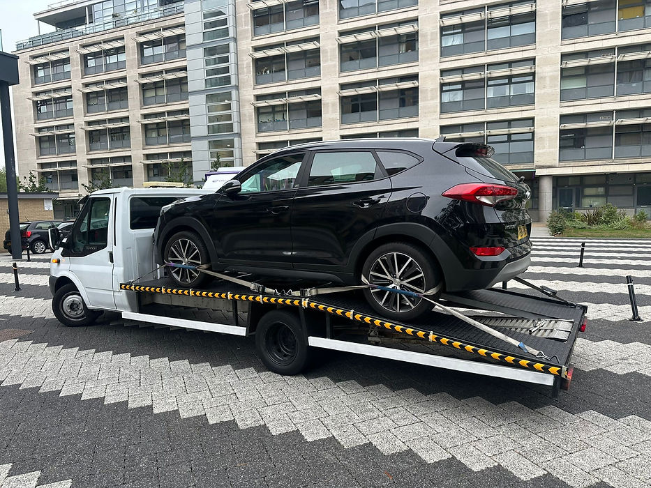 Black Hyundai Tucson SUV strapped to a white flatbed recovery vehicle on a patterned road