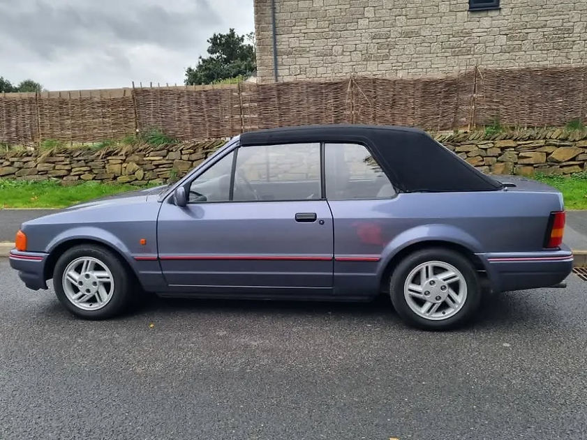 Blue classic convertible car parked on a road with stone wall backdrop
