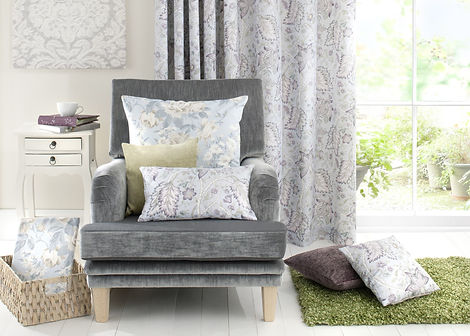 A living room with a gray armchair, floral pillows, and drapes