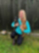 A blonde woman kneels smiling and holds two miniature Dachshunds in front of a dark wooden fence