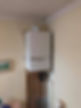 Wall-mounted white boiler in a home interior, fitted above pipes on a cream wall
