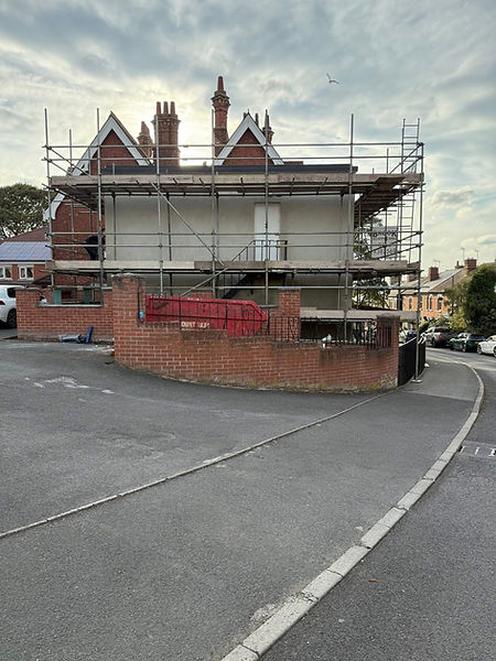 House with full front scaffolding, low brick wall and paved road in front
